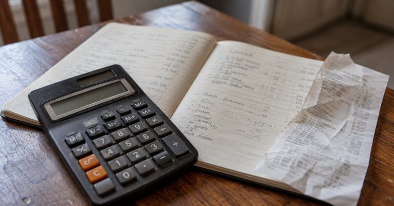 A calculator and shopping receipt on an open household notebook.